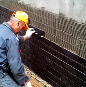 Мастер укладывает керамогранитную плитку на стены цокольного этажа